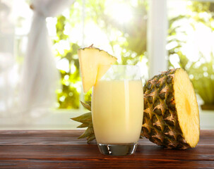 Tasty pineapple cocktail or smoothie in glass and fresh fruit on wooden table indoors. Space for...