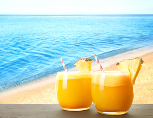 Tasty pineapple cocktail in glasses on wooden table against seascape. Space for text