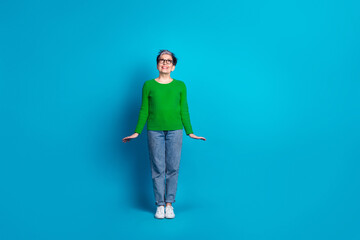 Elderly woman with bright smile in green sweater stands against blue backdrop showcasing joy and style