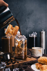 Hand of barista pours refreshing iced coffee into a glass capturing the perfect vertical shot with crispy snacks for coffee lovers.