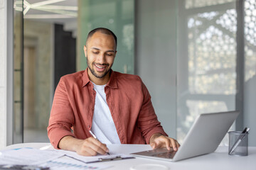 Portrait of a young successful financier, a man behind paperwork, filling out tax forms, and...