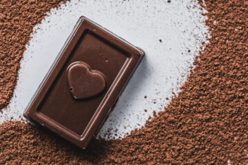 Chocolate with heart shape on cocoa powder background, sweet food concept.