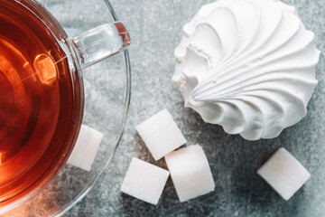 Cup of tea with marshmallow and sugar cubes on grey background.