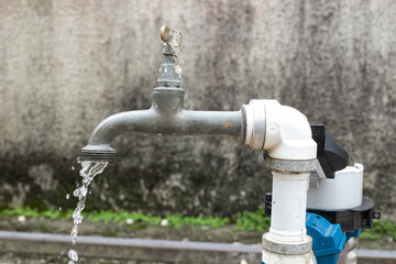 Water tap with the focus on its spout. The photo has neutral colors and water comes out of the hole.