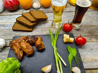 Fried chicken pieces lie on a sliced board next to glasses of beer