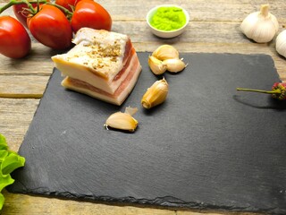 Juicy piece of lard on a sliced ​​granite board surrounded by vegetables and greens