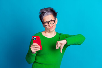 Elderly woman with smartphone showing disapproval gesture against a vibrant blue background