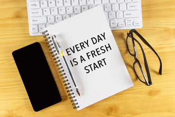 White notepad with text Every day is a fresh start lying on laptop on wooden table.