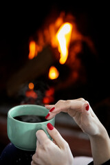 A female hand holding a cup of coffee near a fireplace