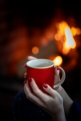 A female hand holding a cup of coffee near a fireplace