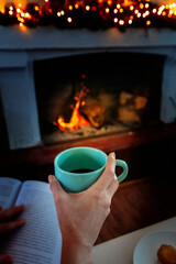 A female hand holding a cup of coffee near a fireplace