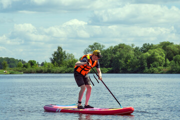 A man in life jacket on sap board on the river paddling along the river.