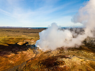 Tourists walking along a wooden path observe a plume of smoke rising from the geothermal area of Grindavik, captivated by the natural spectacle unfolding before them