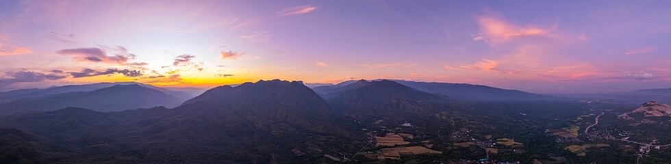 Obraz premium A breathtaking view of a colorful sunset over layered mountain silhouettes, with warm hues of orange, pink, and blue blending seamlessly across the sky.