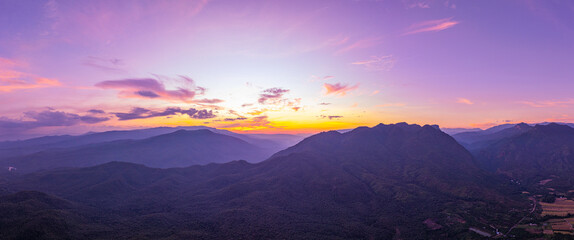 A breathtaking view of a colorful sunset over layered mountain silhouettes, with warm hues of orange, pink, and blue blending seamlessly across the sky.