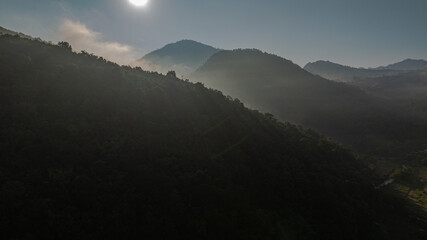  Aerial view of the sun above The sun over the mountain peaks shines through the valley. Cloudy skies and surrounding hills enhance the peaceful ambiance of this scenic setting.