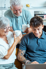 Obraz premium Grandparents and grandson spending quality time in a cozy home during the holidays, sitting together on the couch, holding cups of tea, smiling, laughing, and sharing joyful stories in a relaxed