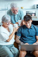 Obraz premium A family scene with grandparents and a grandson in the living room, the boy teaching them how to use the internet on a laptop while they share tea and bond over learning new skills