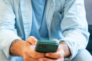 Close up of man hands messaging on mobile phone to communicate and chat with people remote. Concept of social media and technology. Casual wear. Using cell to write friends and work at home
