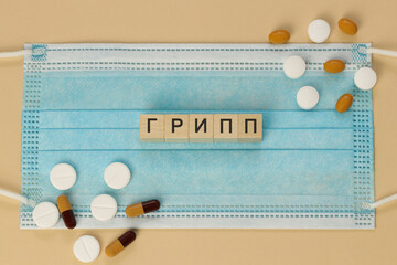 Грипп - Influenza in Russian, spelled with wooden cubes on a surgical mask, surrounded by pills.   Written in Cyrillic also in languages such as Bashkir, Kyrgyz, Tatar, and Yakut.