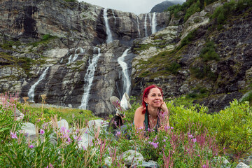 Happy woman enjoying her free time while lying on grass in the mountains, waterfalls background