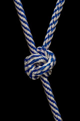 Detailed look at a blue and white braided rope knot against a black background focusing on craftsmanship and texture