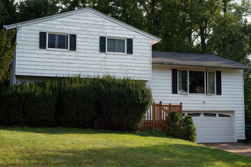 A split-level house with peeling paint on the aluminum siding and overgrown bushes in front