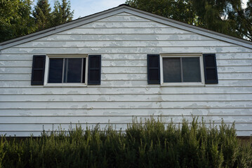 Detail of peeling paint on the aluminum siding on the upper level of a split-level house