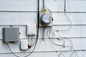 Electrical, cable, and phone inputs on the outside of an aluminum-sided house