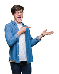 Young handsome man wearing glasses over isolated background amazed and smiling to the camera while presenting with hand and pointing with finger.