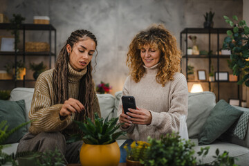 female friends photographing flower pot with mobile phone at home