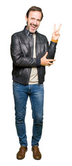 Obraz premium Middle age handsome man wearing black leather jacket smiling with happy face winking at the camera doing victory sign. Number two.