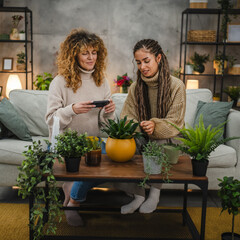 female friends photographing flower pot with mobile phone at home