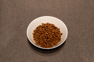 A close-up of a hand pouring dry pet food into a white bowl. The image showcases brown crunchy kibble pieces falling, emphasizing pet care and feeding routines. Perfect for pet food advertisements, an