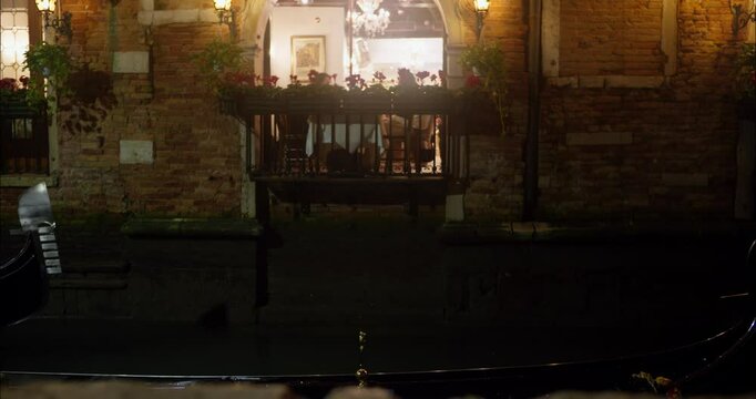 People dining at a restaurant in Venice while a gondola passes by