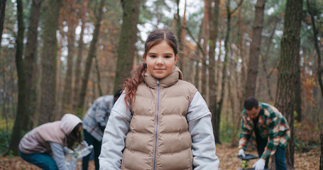Front camera view of little Caucasian girl standing in front of group of people. Child looking at...
