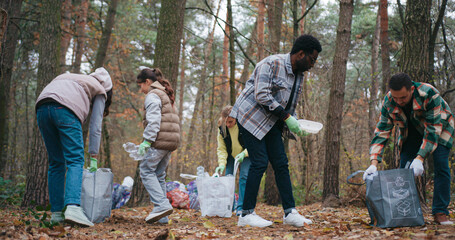 Family cleaning up forest from plastic and other trash. Everyone picking up pieces of rubbish and...