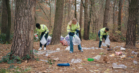 Warm moment of group of volunteers working as team by cleaning up forest from trash laying on...