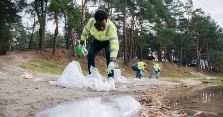 View from below of African American man with glasses working at beach. Wearing green gloves for...