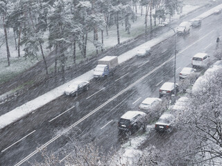 View from the window over heavy fluffy snow falling over the street with cars parked along the roadside and urban park with green grass on  a snowy winter day in Kyiv, Ukraine.