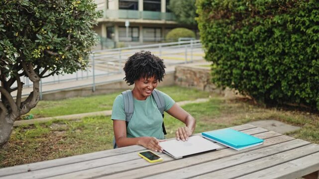 Young student opening laptop and smiling in slow motion. Young student smiling while opening a laptop at a picnic table on campus, enjoying a moment of connection and learning
