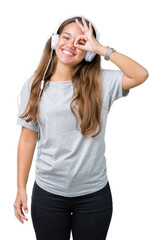 Naklejka premium Young beautiful woman wearing headphones listening to music over isolated background doing ok gesture with hand smiling, eye looking through fingers with happy face.