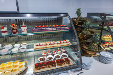 Variety of colorful desserts with strawberries, cream, and pineapple displayed behind glass counter at buffet station. Curacao.