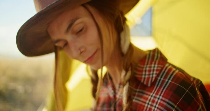 A young musician happily enjoys playing the ukulele inside a bright yellow camping tent surrounded by nature