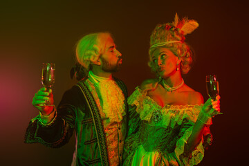 Elegant couple in vintage costumes celebrating with champagne in dramatic lighting