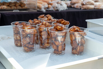 Portion size clear plastic containers filled with soft crispy golden brown bite size pretzels. The cups are in a white tray for sale at a farmers' market. The sweet and salty snack is freshly baked.