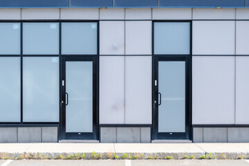 Two single glass doors with frosted windows and black trim in a ground level modern building.The exterior wall is light grey metal panels. There are frosted glass windows in the commercial storefront.