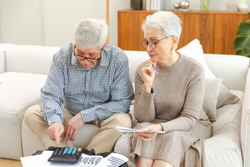 Middle aged senior couple sit with laptop and paper document. Older mature man woman reading paper...