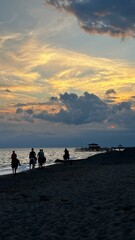 Silhouetted horseback riders travel along the sandy shoreline as the sun sets, casting a golden...