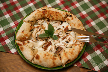 a delicious chicken and mushrooms pizza on tablecloth , sliced served on a wooden board with a tablecloth